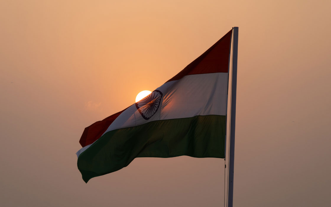 Wehende Flagge von Indien vor einem Sonnenaufgang. Der Himmel ist in orange getränkt