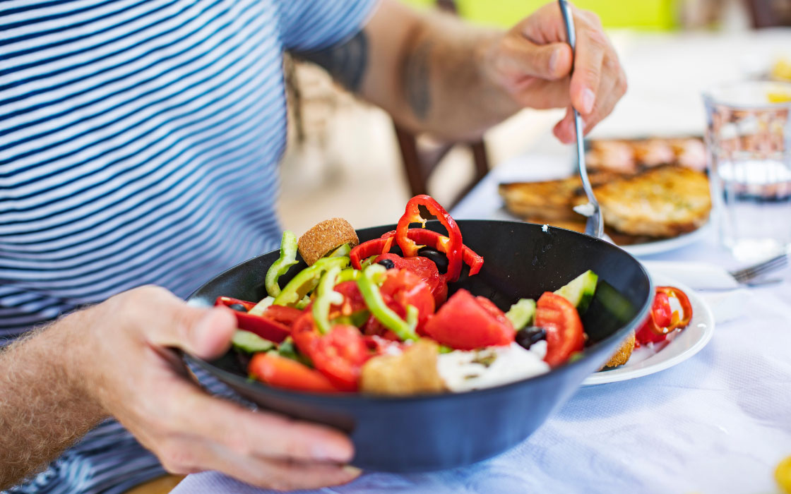 Mann tischt griechischen Salat auf.